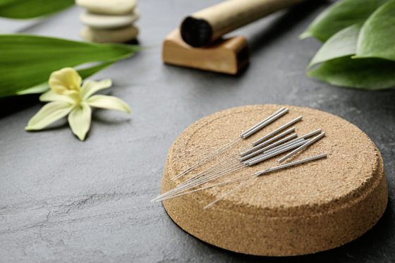 Cork coaster with acupuncture needles on black table. Space for