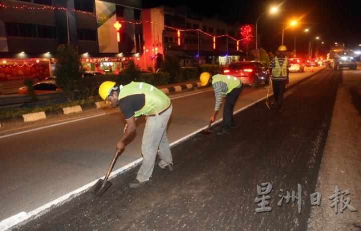 铺路工程的每一道工序都需要认真完成，否则会影响铺路质量。图中铺工们正在铲去不要的沥青碎石尘土。